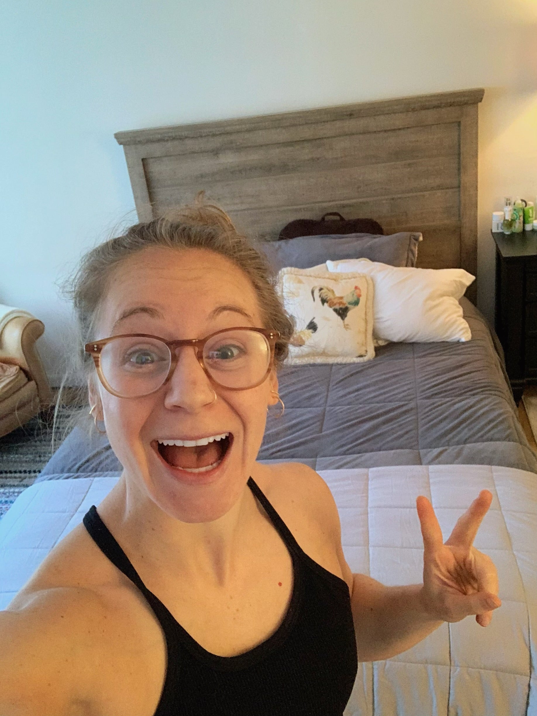 selfie of young fit woman making a peace sign in front of bed